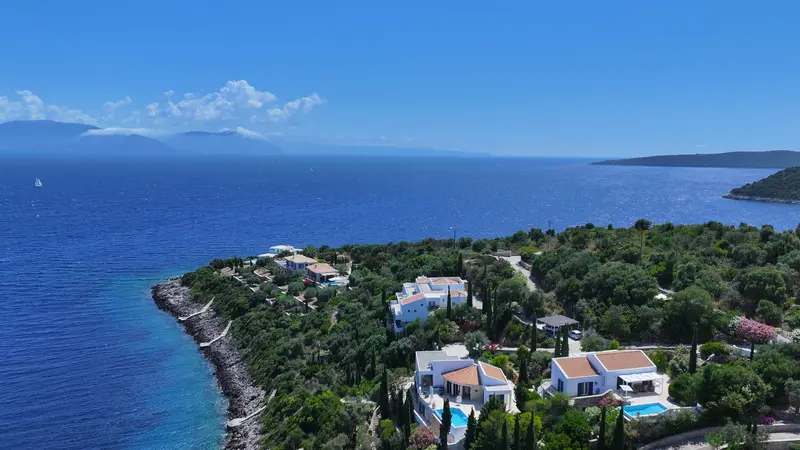 High aerial of the Syvota headland, the estate among olive trees at the water, open blue sea with a lone sailboat