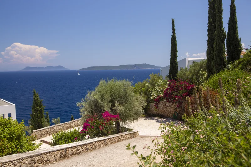 Stone path descending through bougainvillea and cypress towards the sea and the islands