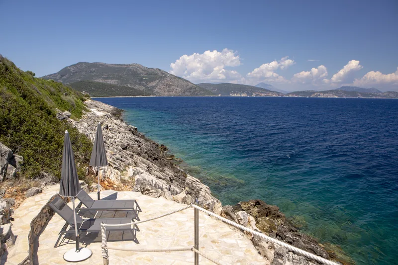 Two closed parasols and loungers on the stone sea terrace above the rocks, the coast beyond
