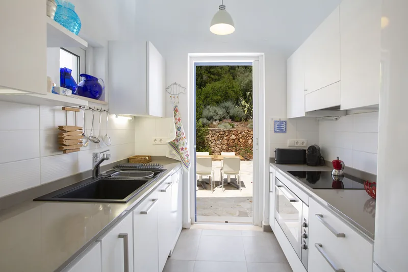 Narrow white kitchen with stone worktops and a door opening to a shaded garden dining table