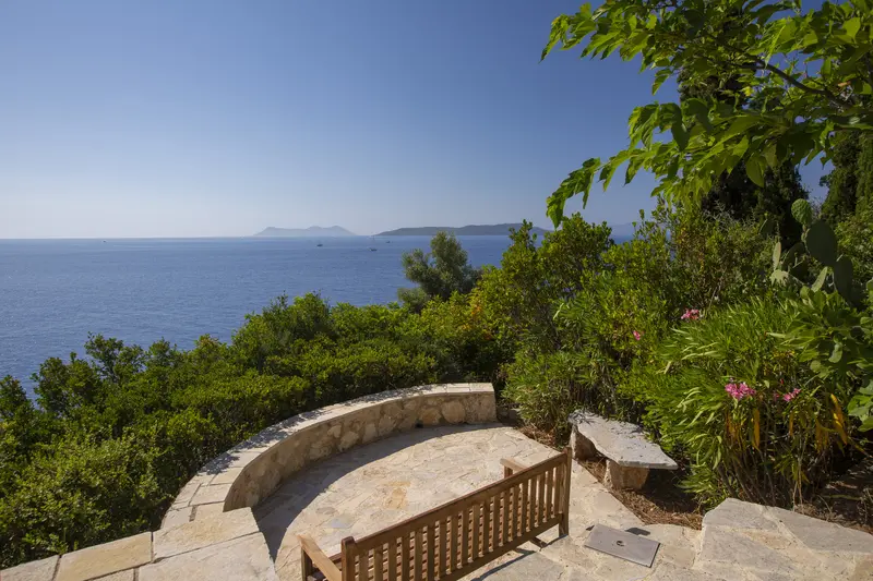 Clifftop stone belvedere with a curved bench facing the open Ionian and island silhouettes