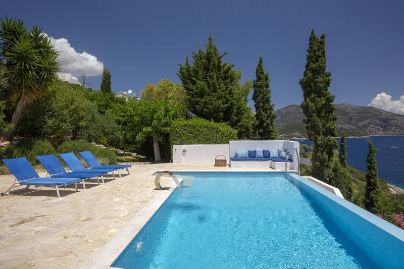 Sun loungers on flagstones beside the pool, the sea filling the horizon