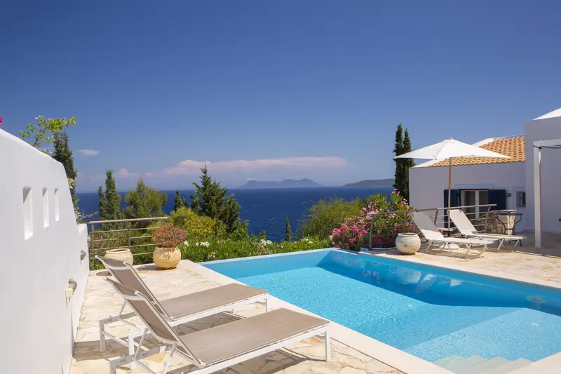 Loungers on the stone pool terrace with pink bougainvillea at the infinity edge and islands on the horizon