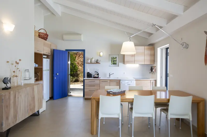 Kitchen and dining room with pale oak cabinetry and a cobalt blue plank door open to the garden