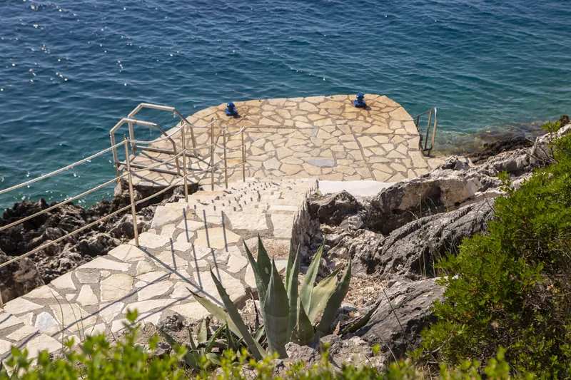 The private stone swimming platform at the water’s edge with an iron railing and agave
